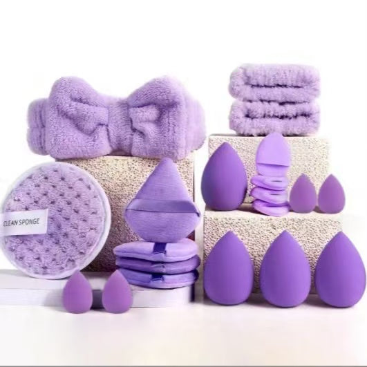 Set of purple beauty tools including sponges and a towel on a white background